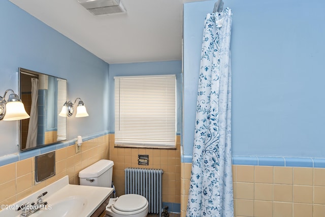 bathroom featuring toilet, radiator, a wainscoted wall, tile walls, and visible vents