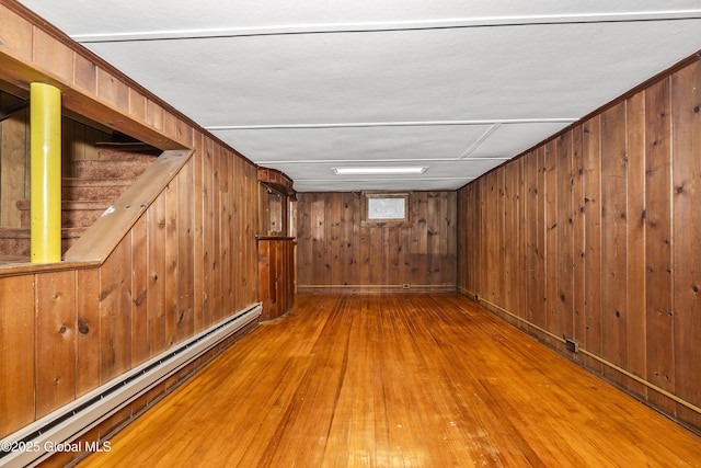 below grade area featuring stairway, baseboard heating, wood walls, and hardwood / wood-style floors