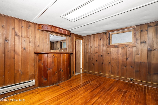 unfurnished room featuring wood walls, baseboard heating, and hardwood / wood-style flooring