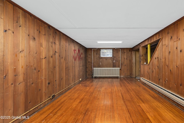 below grade area with radiator heating unit, a baseboard heating unit, wood walls, and hardwood / wood-style floors
