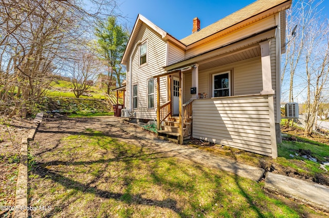 rear view of property with a porch, a shingled roof, and a chimney