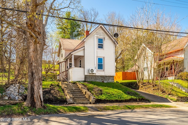 view of front facade featuring covered porch, a chimney, ac unit, fence, and stairs