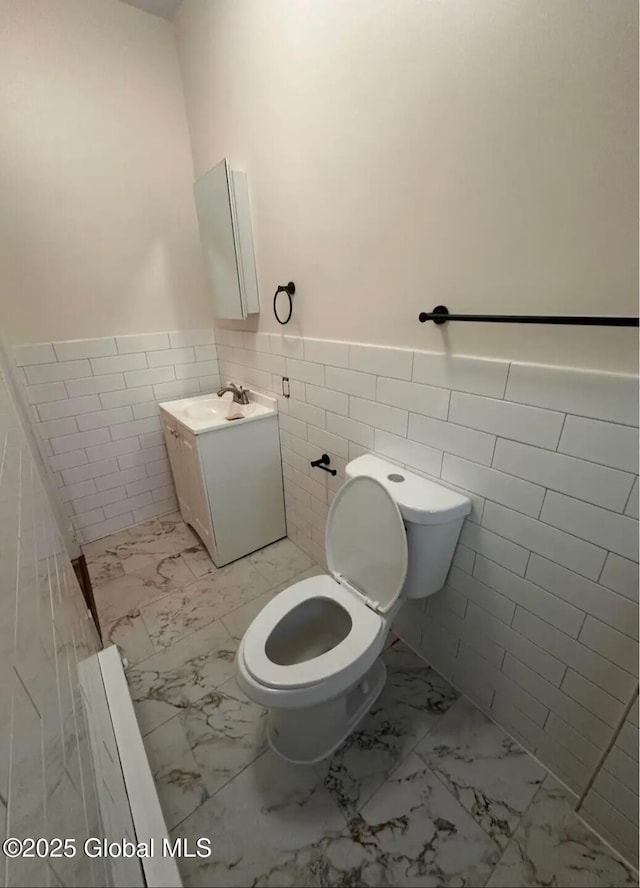 28 Pulaski St, Amsterdam, NY 12010 - half bath featuring vanity, marble finish floor, toilet, tile walls, and a wainscoted wall