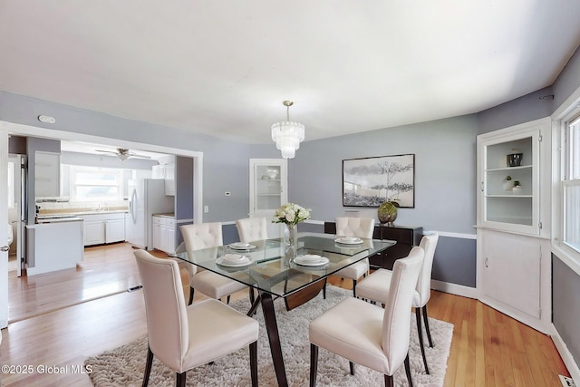 dining space featuring light wood-style floors, baseboards, and ceiling fan with notable chandelier
