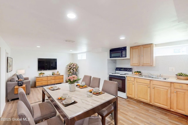 kitchen with light brown cabinetry, black microwave, a sink, light wood-type flooring, and range with electric stovetop