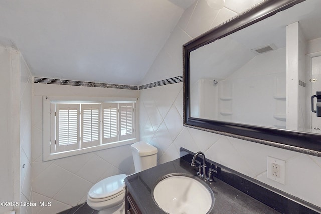 bathroom featuring visible vents, vanity, lofted ceiling, toilet, and tile walls