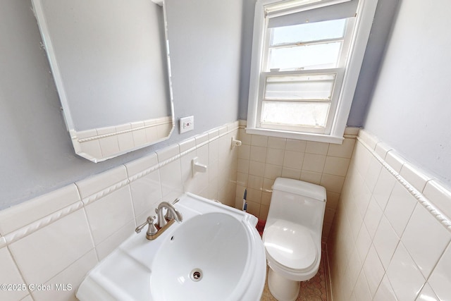 bathroom featuring toilet, tile walls, a sink, and a wainscoted wall