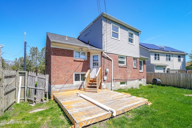 back of property featuring a lawn, a deck, brick siding, a fenced backyard, and entry steps