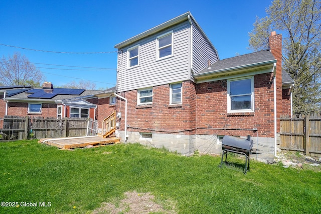 back of property featuring a lawn, brick siding, a chimney, and a fenced backyard