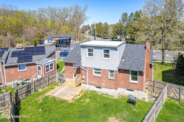 back of house with roof with shingles, brick siding, a fenced backyard, a chimney, and a yard