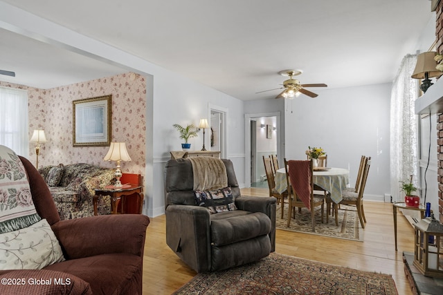 living area featuring baseboards, a ceiling fan, wallpapered walls, and light wood-style flooring