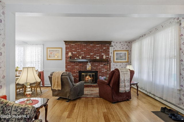 living room featuring baseboard heating, a fireplace, light wood-style flooring, wallpapered walls, and a baseboard heating unit