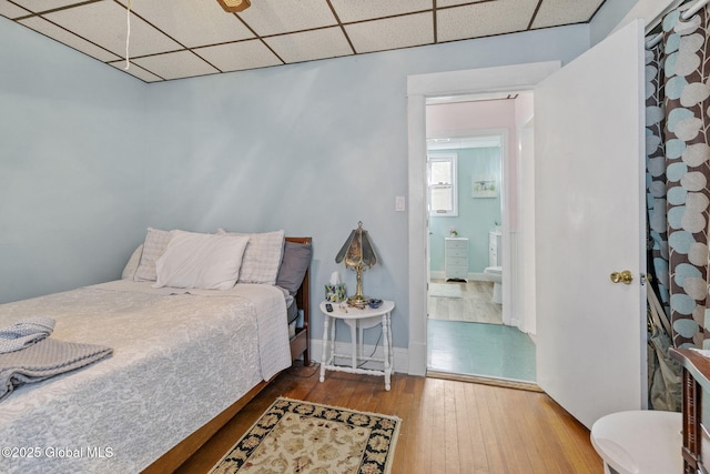 bedroom with baseboards, a paneled ceiling, and hardwood / wood-style floors