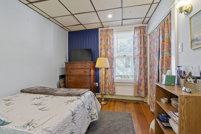 bedroom with a baseboard heating unit, multiple windows, a paneled ceiling, and wood finished floors