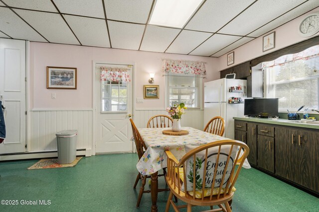 dining room with a baseboard heating unit, tile patterned floors, a drop ceiling, and wainscoting