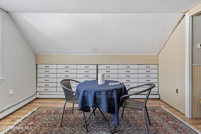 dining area featuring wooden walls, vaulted ceiling, light wood-style flooring, and a baseboard radiator