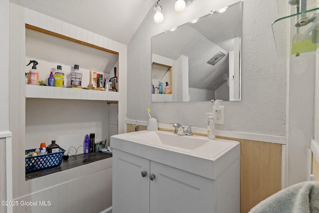 bathroom with a textured wall, visible vents, wainscoting, and vanity