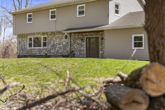view of front of home featuring a shingled roof, stone siding, and a front lawn