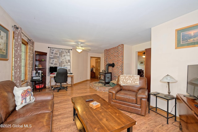 living room featuring baseboards, a ceiling fan, wood finished floors, and a wood stove