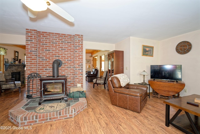 living room with a fireplace, a ceiling fan, a wood stove, and wood finished floors