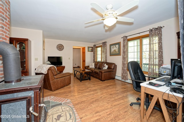 office space featuring ceiling fan, a wood stove, baseboards, wood finished floors, and a baseboard radiator