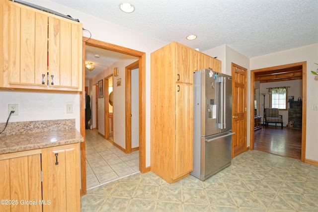 kitchen featuring light brown cabinets, light stone countertops, baseboards, high quality fridge, and a textured ceiling