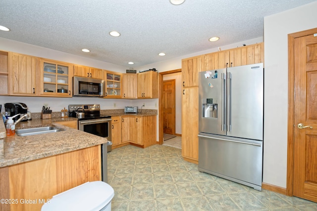 kitchen featuring appliances with stainless steel finishes, a sink, a textured ceiling, recessed lighting, and glass insert cabinets