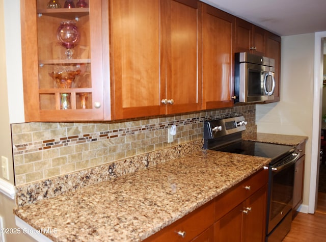 kitchen featuring stainless steel microwave, light stone counters, brown cabinetry, and electric stove