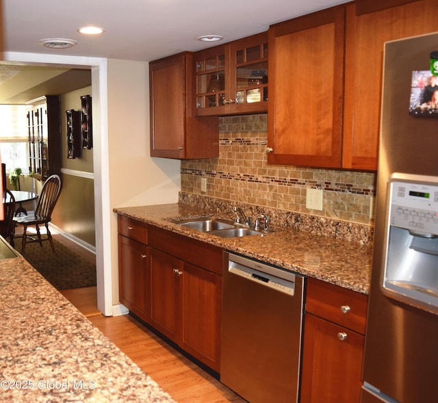 kitchen featuring brown cabinets, tasteful backsplash, a sink, light wood-style flooring, and stainless steel appliances