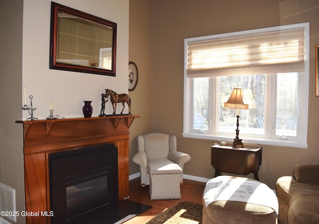 sitting room with baseboards, a glass covered fireplace, and wood finished floors