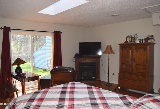 bedroom with access to outside, a textured ceiling, a glass covered fireplace, wood finished floors, and a skylight
