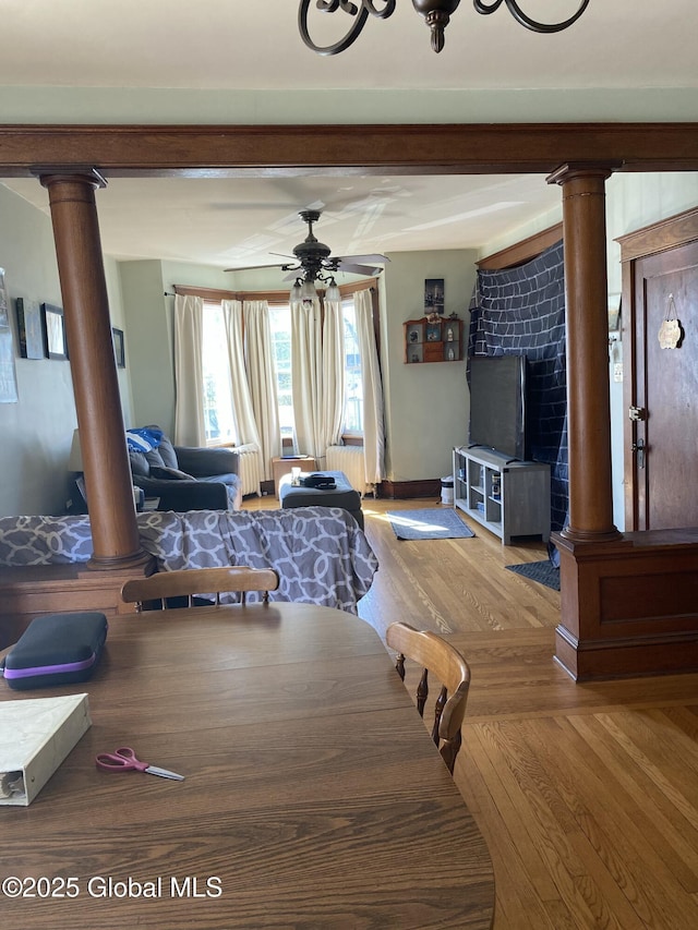 dining space featuring decorative columns, ceiling fan, wood finished floors, and a fireplace