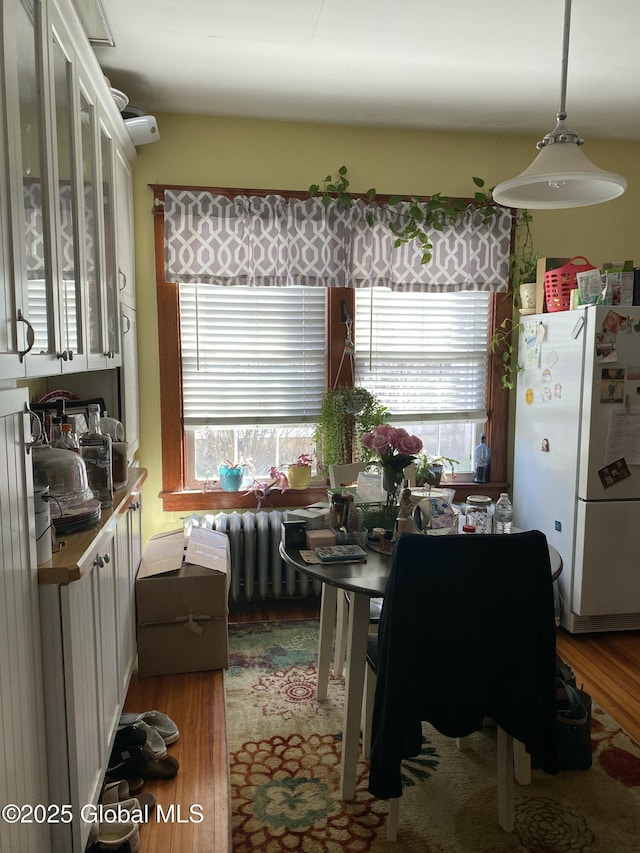 kitchen with freestanding refrigerator, white cabinets, a wealth of natural light, and radiator