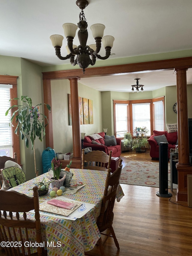 dining room featuring ornate columns, plenty of natural light, wood finished floors, and an inviting chandelier