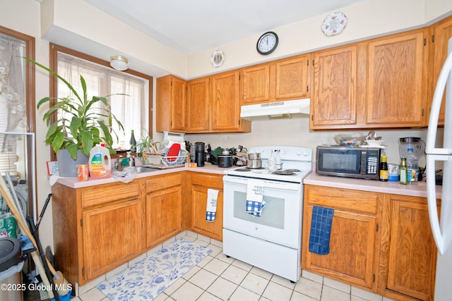 kitchen with brown cabinets, white appliances, light countertops, light tile patterned floors, and under cabinet range hood