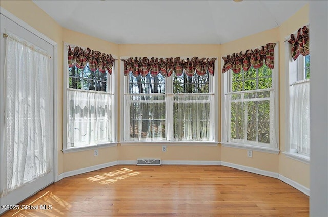 unfurnished sunroom featuring visible vents, baseboards, wood finished floors, and a healthy amount of sunlight