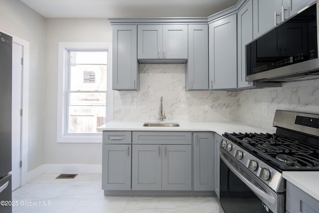 kitchen with stainless steel appliances, gray cabinetry, a wealth of natural light, and a sink