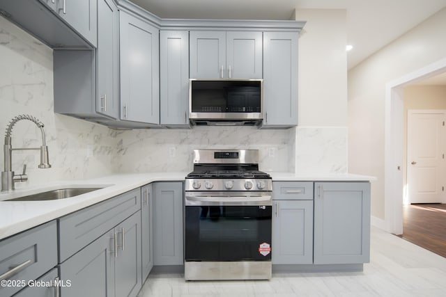 kitchen with light countertops, stainless steel appliances, gray cabinetry, and a sink