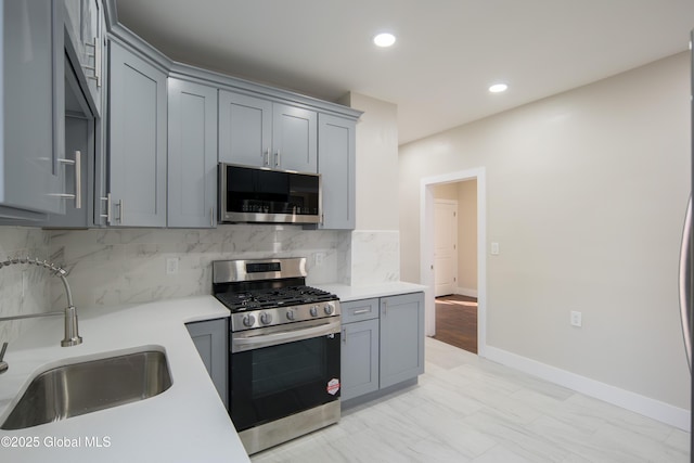 kitchen with gray cabinets, backsplash, appliances with stainless steel finishes, a sink, and light countertops