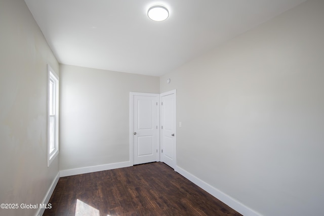 empty room with baseboards and dark wood-type flooring
