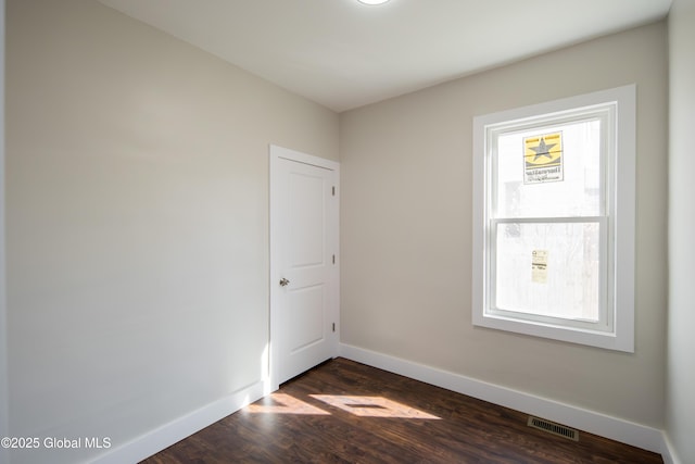 empty room with baseboards, dark wood-type flooring, and visible vents