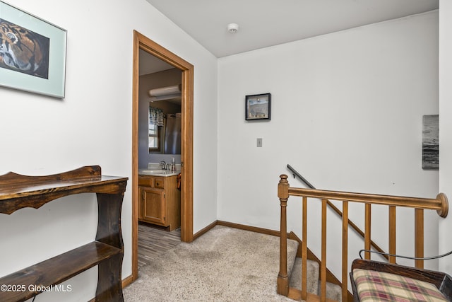 corridor featuring baseboards, a sink, light carpet, and an upstairs landing