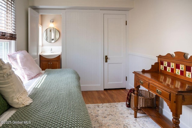 bedroom featuring wood finished floors, a sink, ensuite bath, and a wainscoted wall