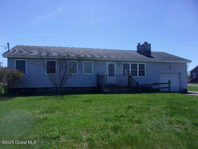back of property featuring a lawn, a garage, and a chimney