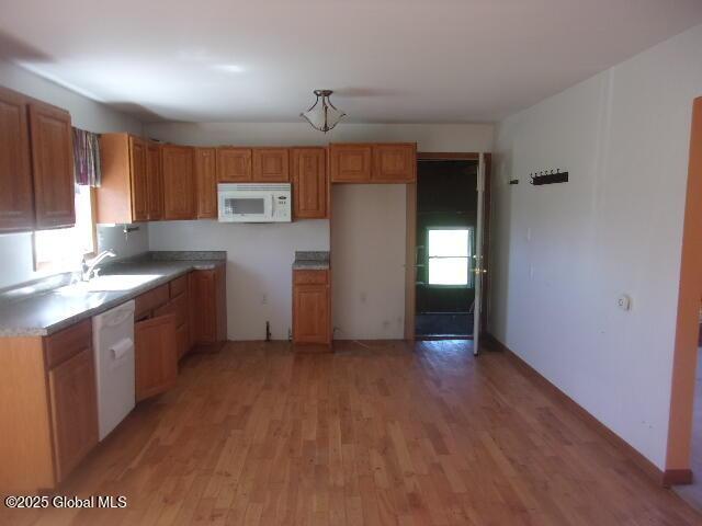 kitchen featuring a sink, light wood-style flooring, brown cabinets, and white appliances