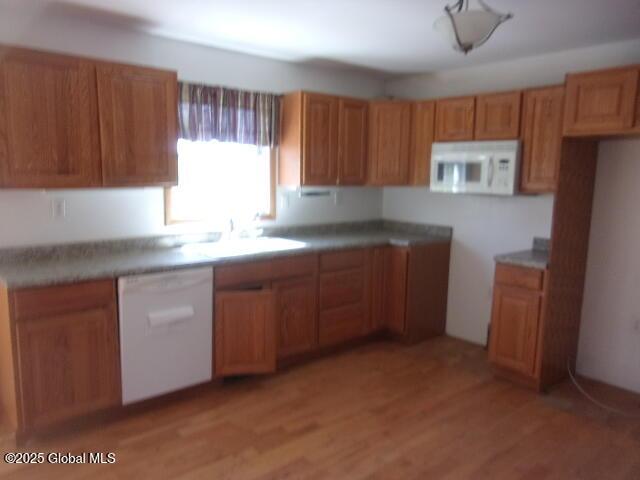 kitchen featuring a sink, brown cabinetry, white appliances, and light wood-style flooring