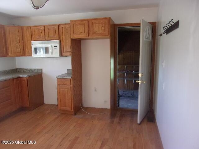 kitchen with light wood-type flooring, brown cabinetry, and white microwave