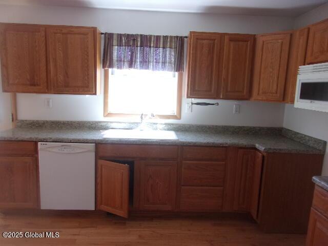 kitchen with a sink, light wood finished floors, brown cabinetry, and white appliances