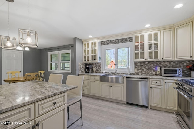 kitchen featuring appliances with stainless steel finishes, cream cabinets, a sink, backsplash, and light stone counters