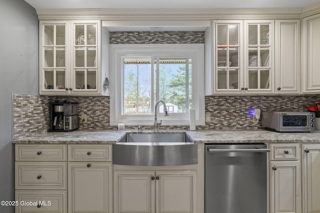 kitchen with dishwasher, a sink, backsplash, glass insert cabinets, and cream cabinets